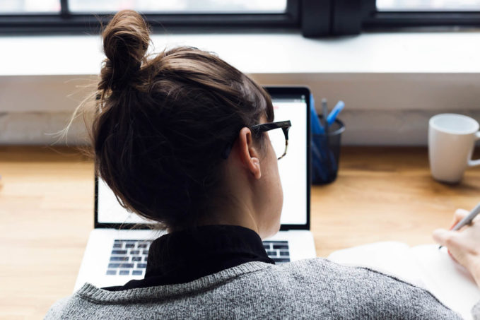 Woman takes notes alongside laptop